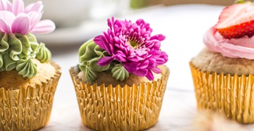 Three cupcakes are wrapped in gold foil with floral icing and edible flowers on top.