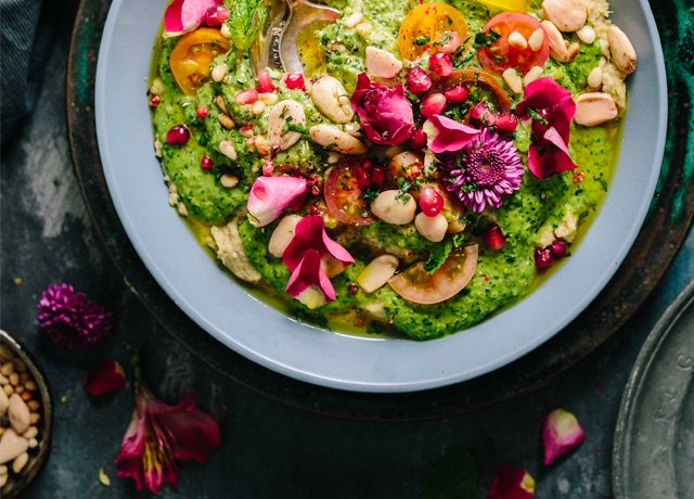 A fresh pesto salad with beans, pine nuts, tomatoes, and edible flowers is on a plate.